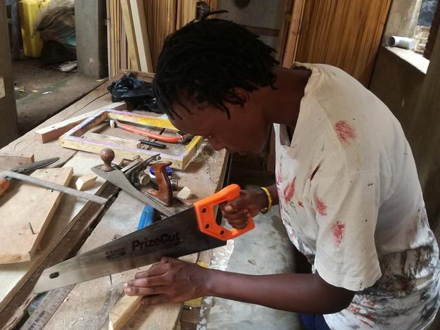 Carpenter cutting a timber board with a handsaw at a workbench